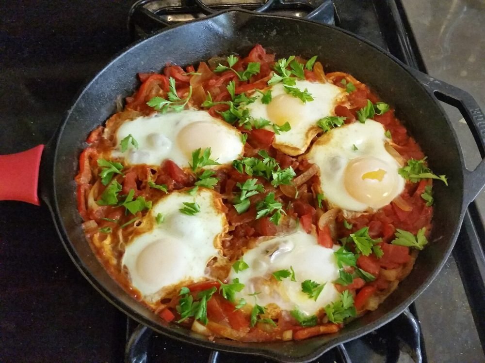 Cazuela con huevos cuajados sobre salsa de tomate y pimientos